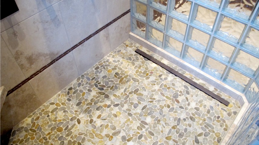 Master shower pan floor with trench drain and glass block. featuring Rivera pebbles gold and durango cross cut 16x16 honed and filled travertine walls. decorative liner bronze copper tan beige
