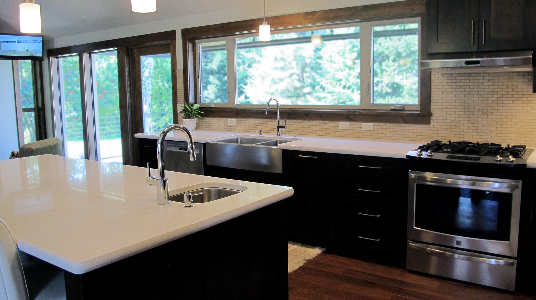 Kitchen island long espresso cabinets full height backsplash stainless steel appliances hardwood engineered dark light counter top quartz prep sink pendant lights window natural light hood 1x2 brick joint natural beige light travertine open concept main floor